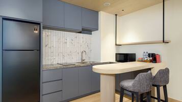 A modern kitchen with grey cabinets, a marble backsplash, a built-in microwave, and a bar area with two stools.