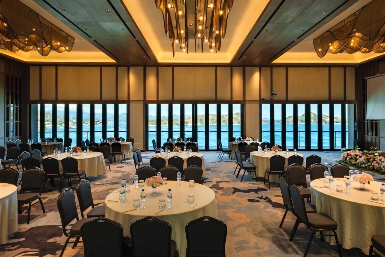 A conference room with round tables, chairs, and a large window overlooking a body of water.