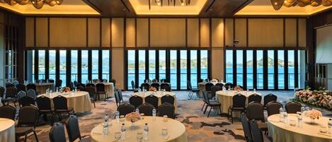 A conference room with round tables, chairs, and a large window overlooking a body of water.
