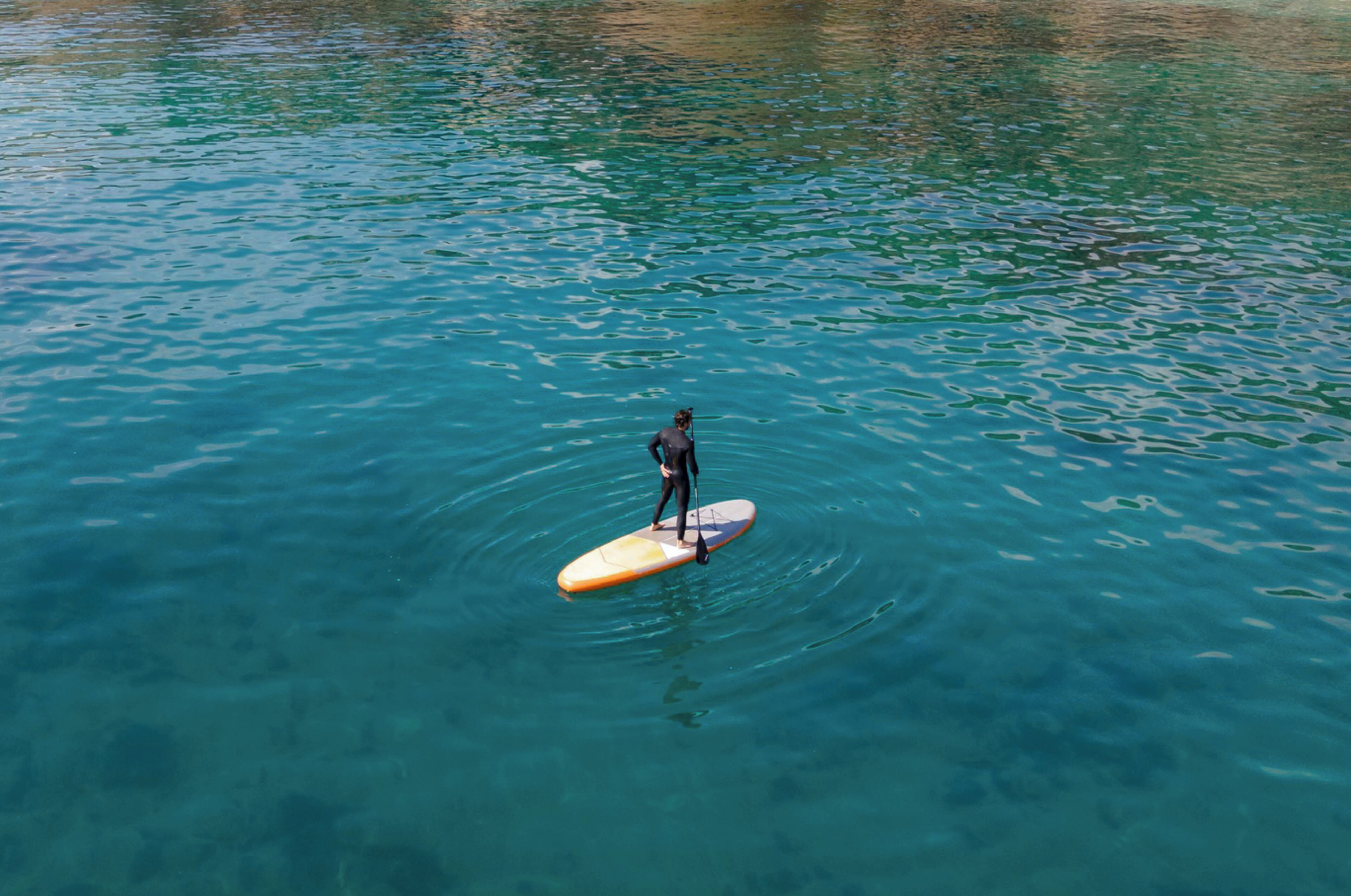 Una persona de pie en una tabla de remo sobre agua cristalina.