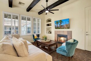 A living room with a beige sofa, a blue armchair, a coffee table, and a fireplace. - Picturesque 1BR in Legacy Villas near Main Pool #A (La Quinta)