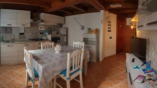 A compact kitchen with white cabinets, a dining table with chairs, a TV, and a 'Welcome' sign. - Vista Sul Pandi Zucchero -HolidayHouse- (Iglesias)