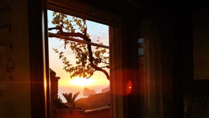 A room with a window overlooking a sunset, a chair, and a small table. - Vista Sul Pandi Zucchero -HolidayHouse- (Iglesias)