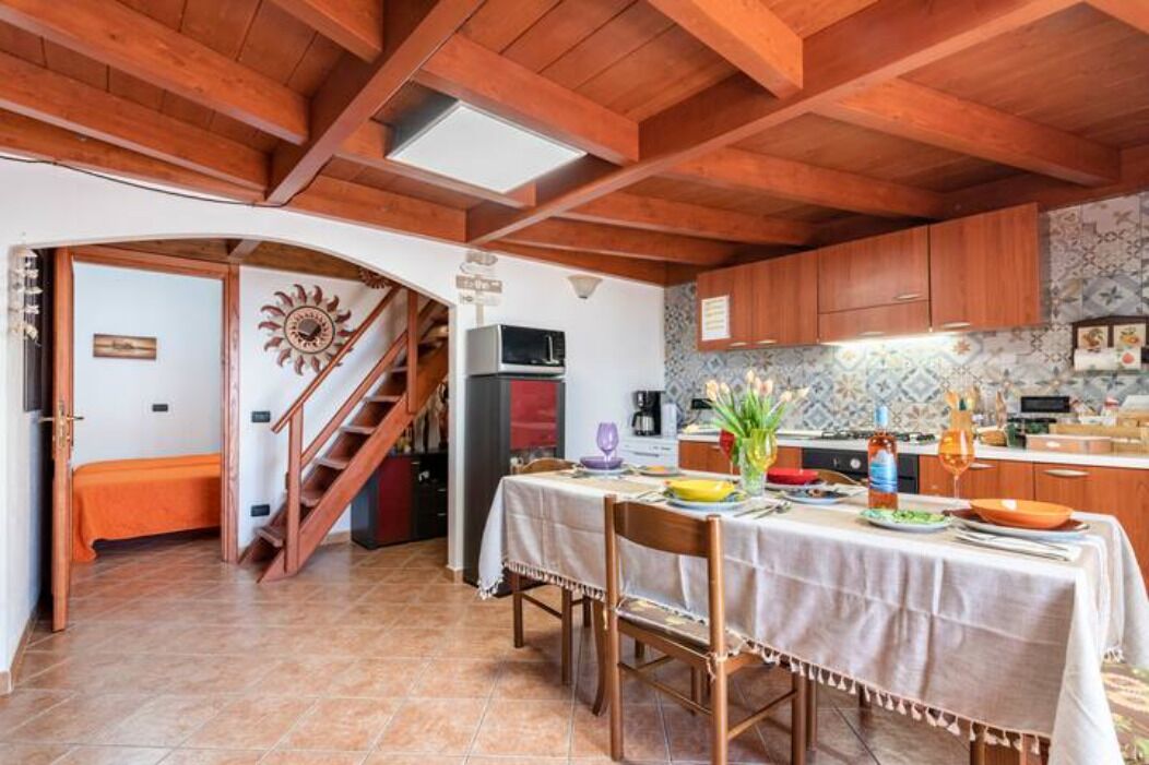 Una cocina acogedora con vigas de madera, una mesa de comedor preparada para dos personas y una escalera que lleva a otra habitación.