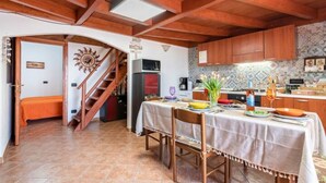 A cozy kitchen with wooden beams, a dining table set for two, and a staircase leading to another room. - Vista Sul Pandi Zucchero -HolidayHouse- (Iglesias)