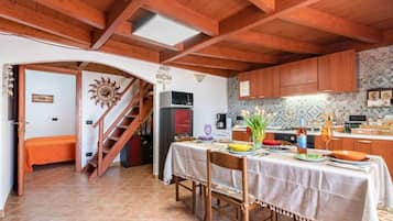 Una cocina acogedora con vigas de madera, una mesa de comedor preparada para dos personas y una escalera que lleva a otra habitación.