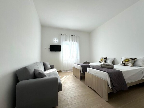 A modern hotel room with a sofa, a bed with a TV, and a window with curtains.