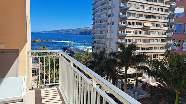 A balcony overlooking a coastal area with a view of the ocean and a building with multiple balconies.