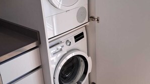 A compact, modern laundry room with a Bosch washer and dryer, built-in cabinetry, and a wooden floor.