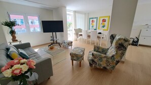 A living room with a sofa, armchair, coffee table, and a TV. There is a dining area with chairs and a table.