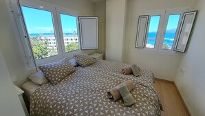 A bedroom with a large bed, two bedside tables, and a view of the sea through large windows.