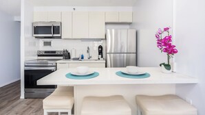 Een moderne keuken met witte kasten, roestvrijstalen apparatuur, een witte eettafel met teal placemats, en een bank.