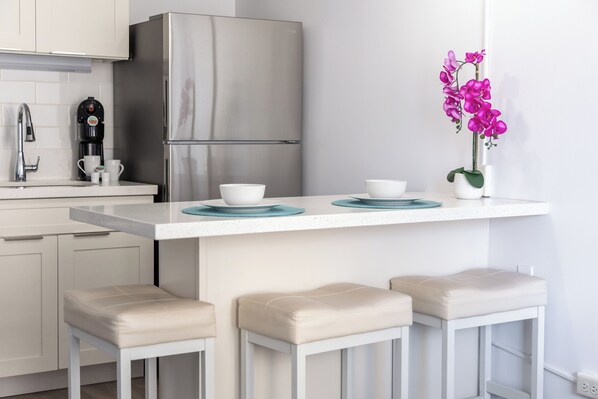 A modern kitchen with a stainless steel refrigerator, a coffee maker, and a small island with stools.