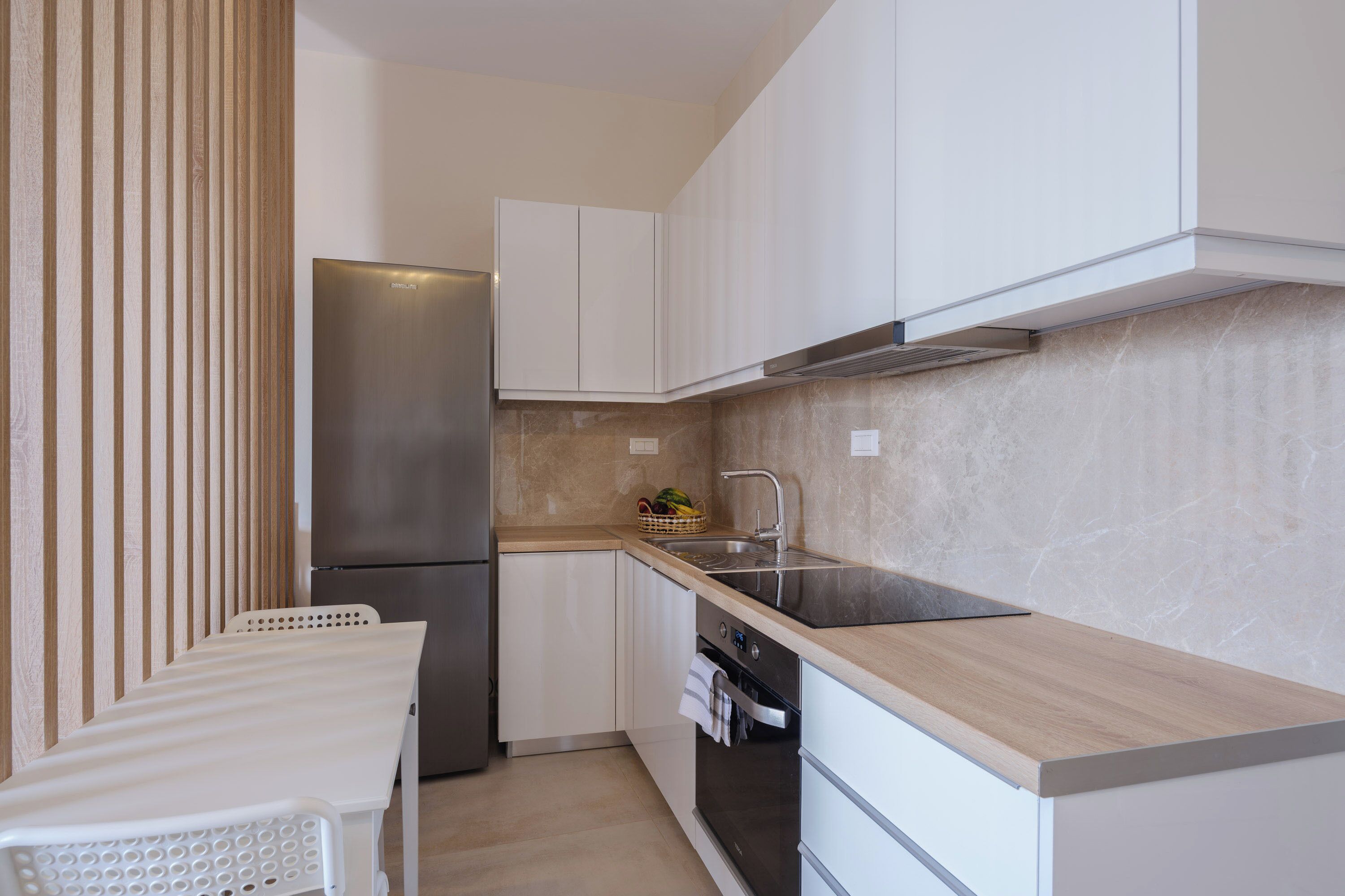 A compact kitchen with white cabinets, a stainless steel refrigerator, a wooden countertop, and a built-in oven.