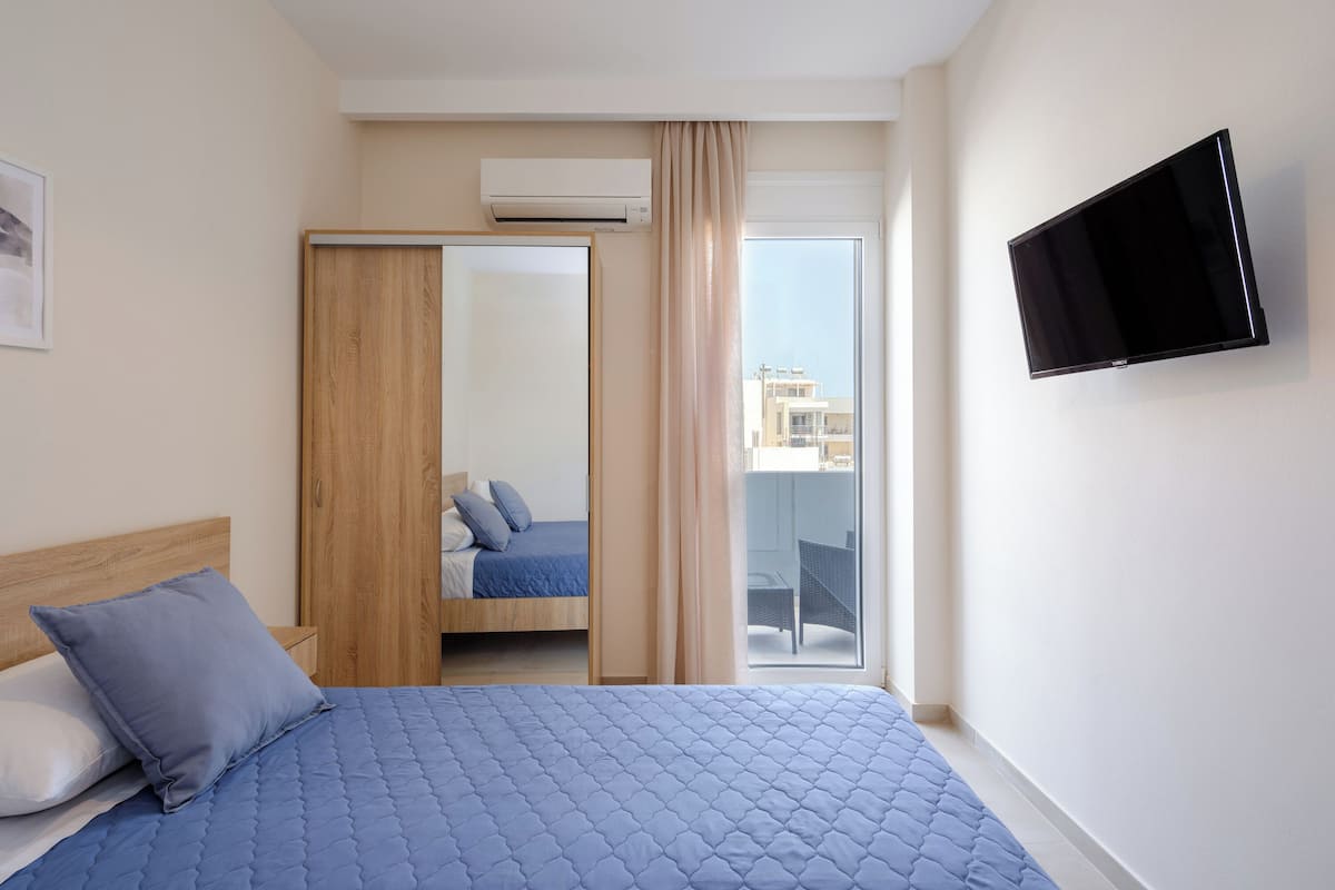 A hotel room with a bed, a TV mounted on the wall, and a sliding door leading to a balcony.