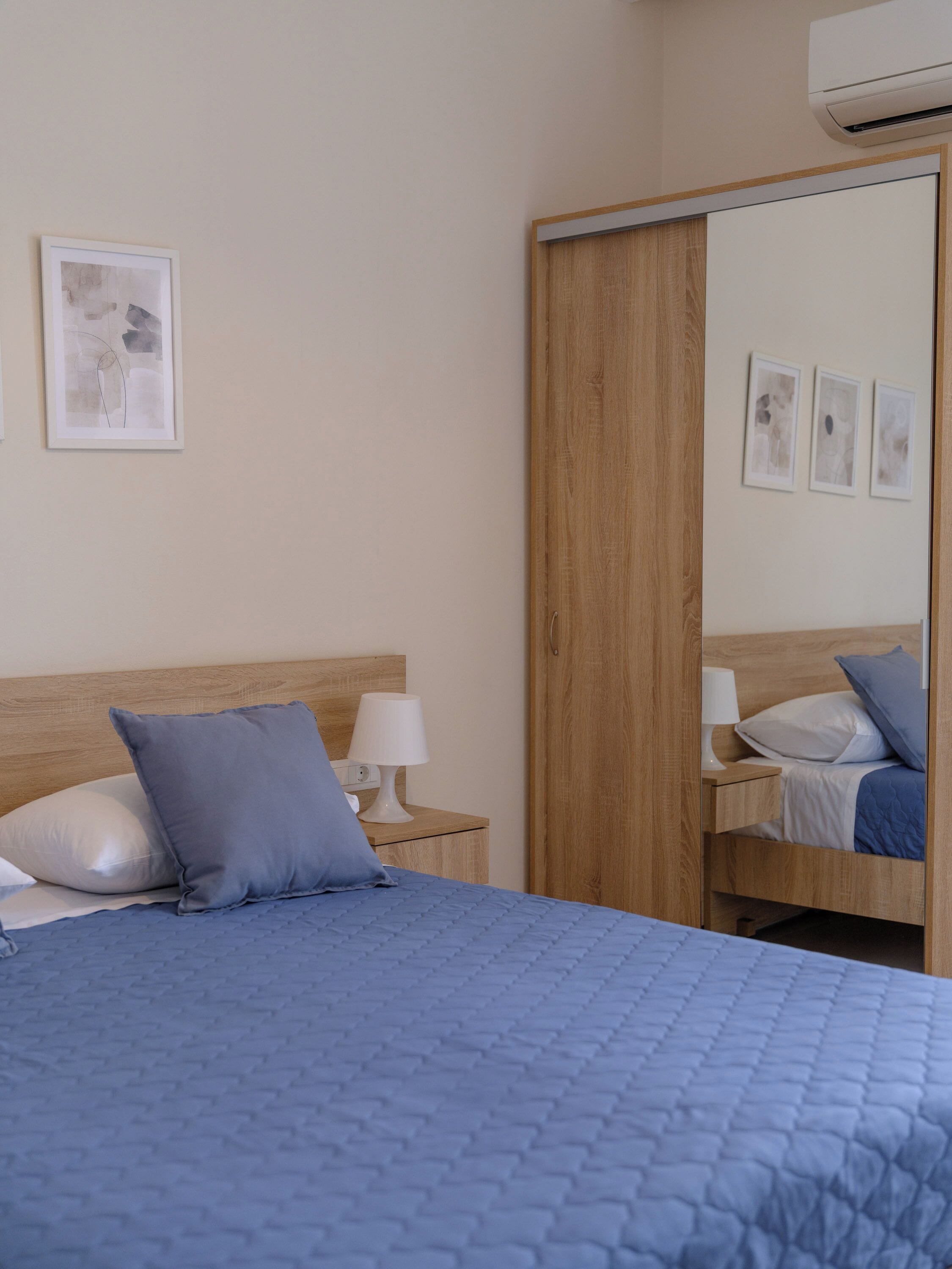 A bedroom with a large bed, a wooden headboard, a nightstand with a lamp, and a wardrobe with a mirror.