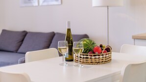 Een eettafel met een fles witte wijn, twee glazen en een mand vol fruit.