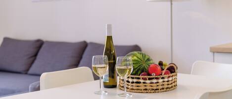 A dining table with a bottle of white wine, two glasses, and a basket of fruits.