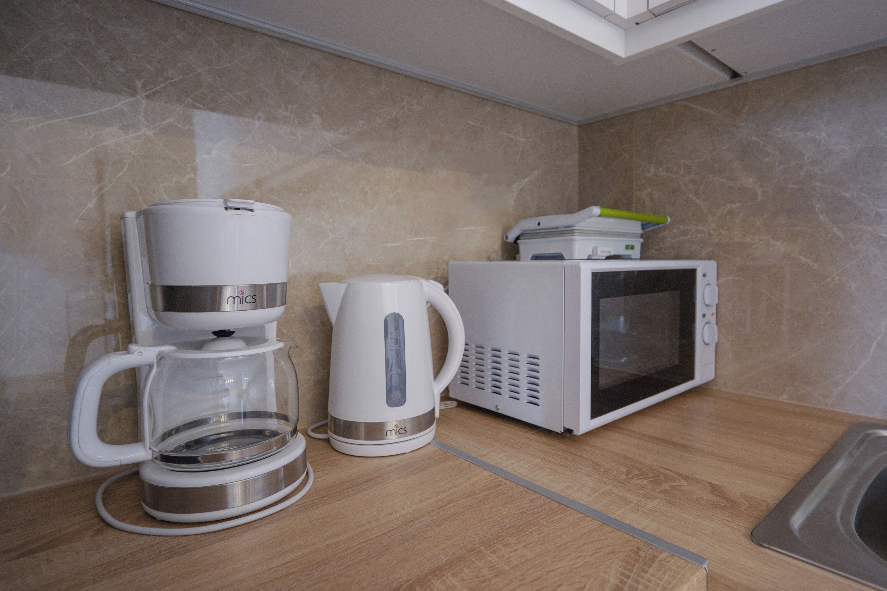 A kitchenette with a coffee maker, a kettle, and a microwave on a wooden countertop.