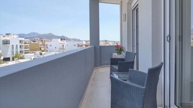 Een balkon met uitzicht op gebouwen en bergen. Er staat een tafel met stoelen en een bloevas.