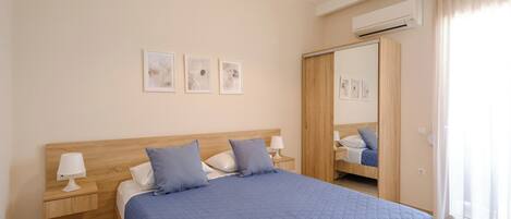 Un dormitorio con cabecera de madera, colcha acolchada azul, dos lámparas de noche y aire acondicionado de pared.