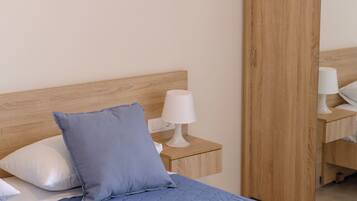 Un dormitorio con cabecera de madera, una cama con colcha azul, una mesita de noche con lámpara blanca y un armario de madera.