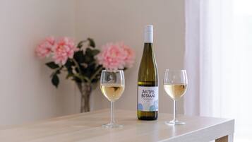 A bottle of wine and two glasses on a wooden table with a vase of flowers in the background.