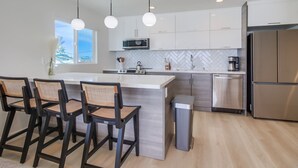 Una cocina moderna con armarios blancos, un refrigerador de acero inoxidable y una isla central con taburetes de bar.