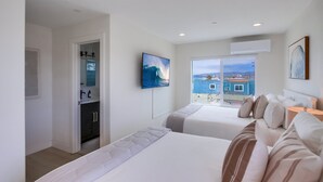 Une chambre d’hôtel avec deux lits, une télévision, une fenêtre donnant sur un immeuble bleu et un appareil de climatisation.