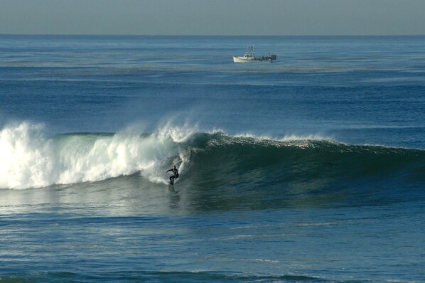 A surfer riding a wave with a boat in the background.