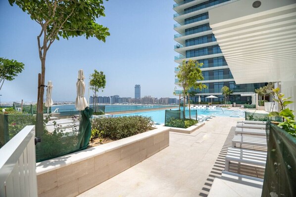 A rooftop pool area with a view of the city skyline, a modern building with balconies, and a clear sky.
