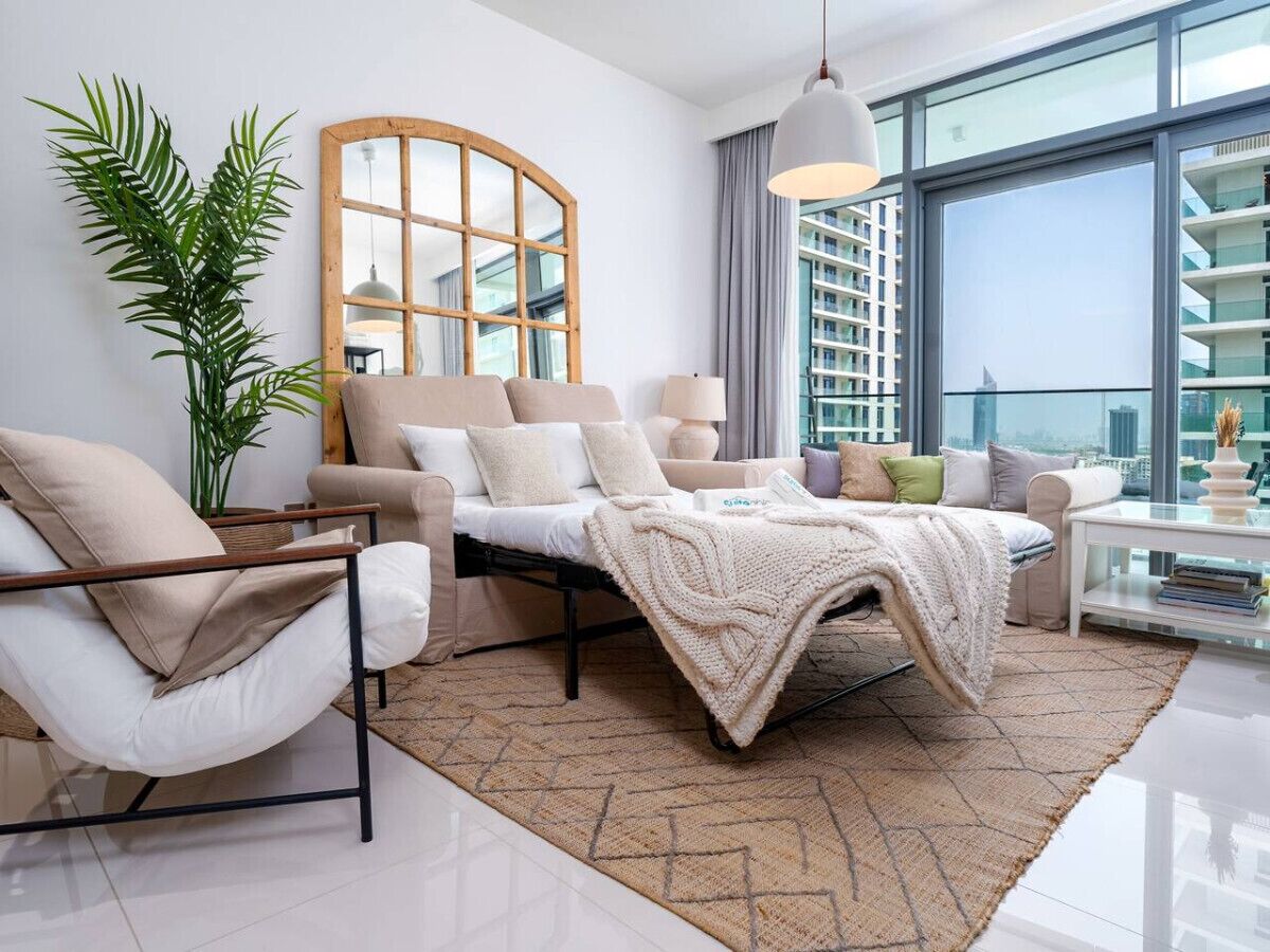 A modern living room with a sofa, armchair, and a large window offering a city view.