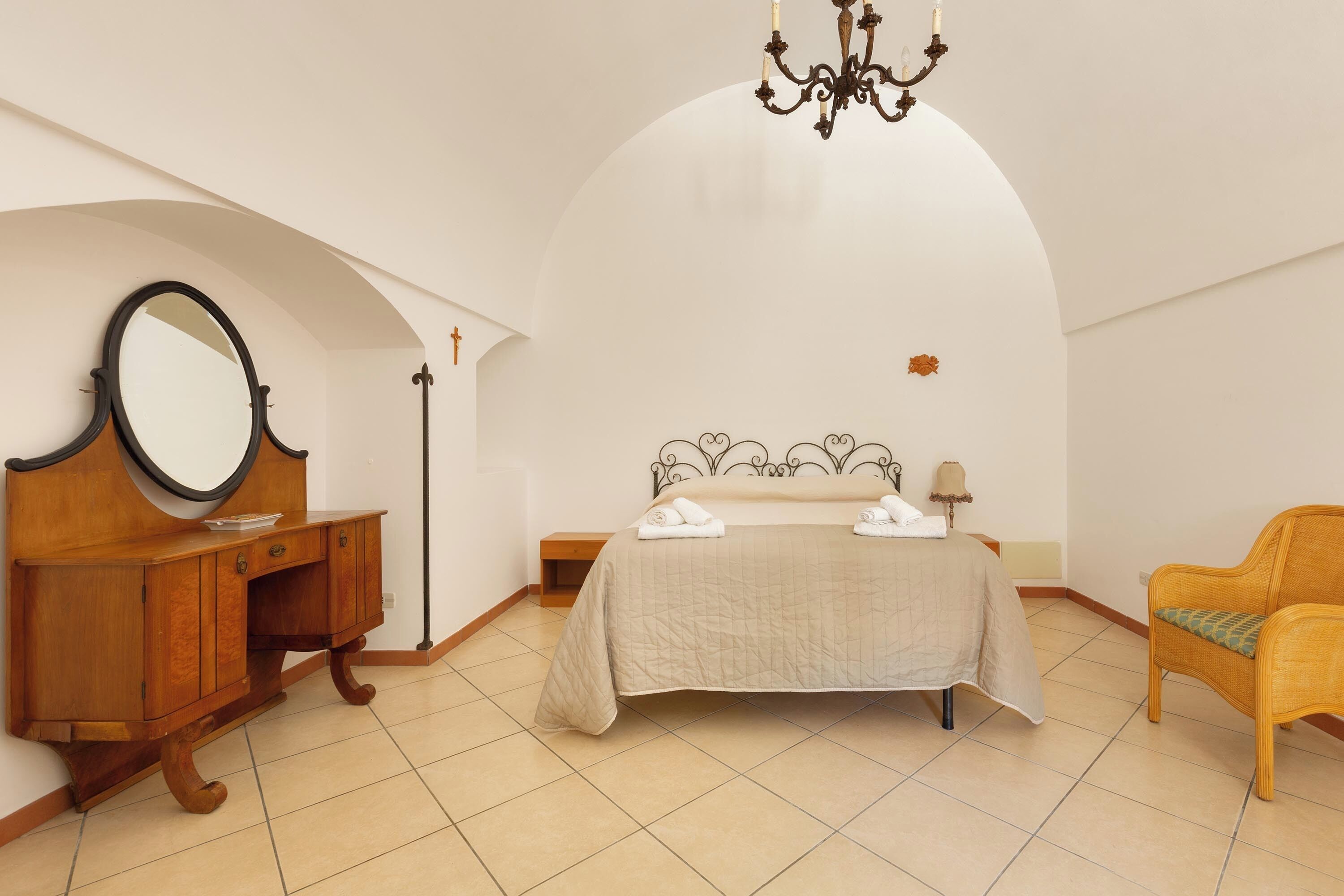 A bedroom with a bed, a wooden dresser, a mirror, a chandelier, and a chair.