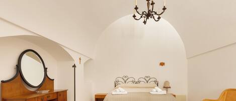 A bedroom with a bed, a wooden dresser, a mirror, a chandelier, and a chair.
