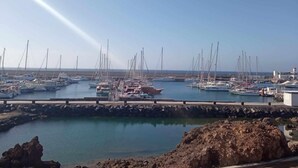 Marina com vários barcos atracados, costa rochosa e céu claro.
