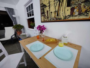 A dining area with a wooden table, two light blue plates, a glass of orange juice, a bowl of yellow flowers, a potted plant, and a painting on the wall. - Golf Course and sea Views With two Terraces! (San Miguel de Abona)