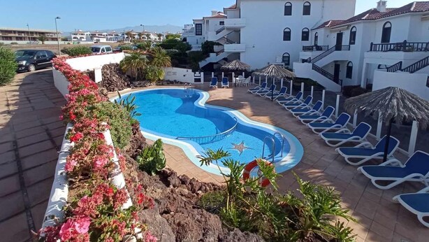 Piscina cercada por espreguiçadeiras e um edifício branco com telhado telhado.