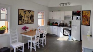 Uma cozinha compacta com armários brancos, uma mesa de jantar com cadeiras e obras de arte nas paredes.