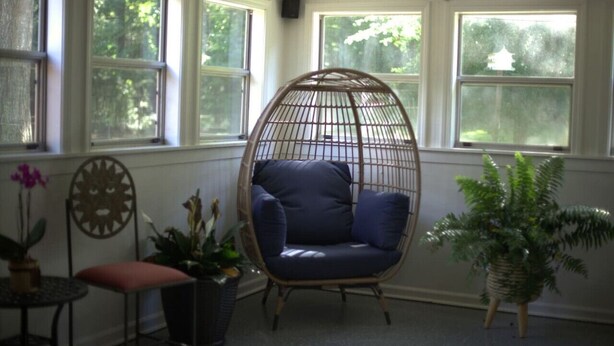 A room with a large window, a wicker chair, a small table with a plant, and a potted plant. - Rest and relaxation in Conyers. (Conyers)