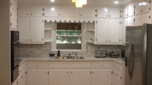 A kitchen with white cabinets, a stainless steel refrigerator, a window with a view, and a tiled backsplash. - Rest and relaxation in Conyers. (Conyers)