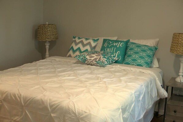 A neatly made bed with a white duvet and patterned pillows, two bedside lamps, and a small bedside table with a lamp.