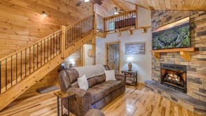 A wooden interior with a staircase, a fireplace, and a mounted television. - Famtastico - Great Deal! Games, Hot Tub, Pets (Morganton)