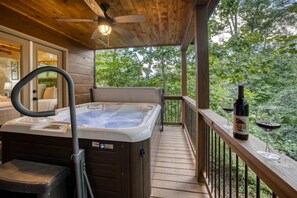 Een houten terras met een jacuzzi, een glas wijn en een fles wijn.