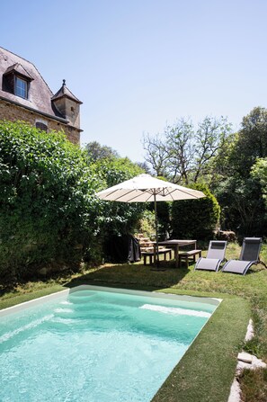 Un jardin avec une piscine, une terrasse en bois et un grand parasol.