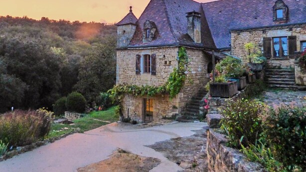 A stone building with a steep roof and a small tower, surrounded by lush greenery. - The Starry Cottage Retreat (Vitrac)