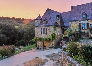 A stone building with a steep roof and a small tower, surrounded by lush greenery. - The Starry Cottage Retreat (Vitrac)