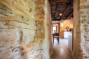 Un couloir aux murs de pierre mène à une cuisine dotée de poutres en bois et d’un décor rustique.