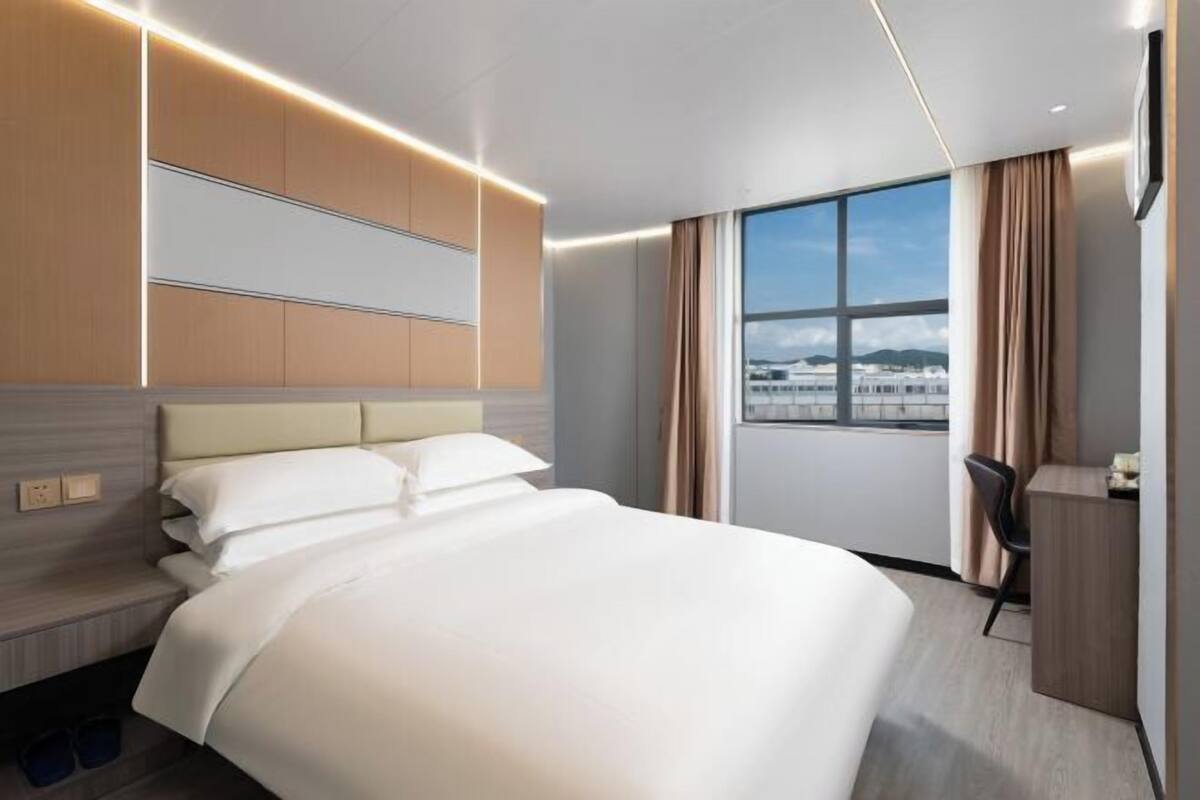 Quarto de hotel moderno com uma cama grande, uma mesa e vista para a cidade.