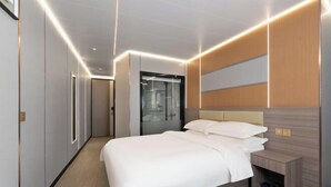 A modern hotel room with a large bed, a bedside table, a mirror, and a wardrobe. - Shenzhen Qiaonan Hotel (Shenzhen)
