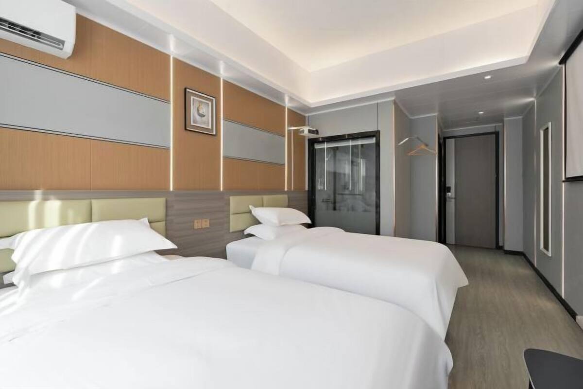 Quarto de hotel com duas camas, um guarda-roupa, um espelho e uma porta para um corredor.